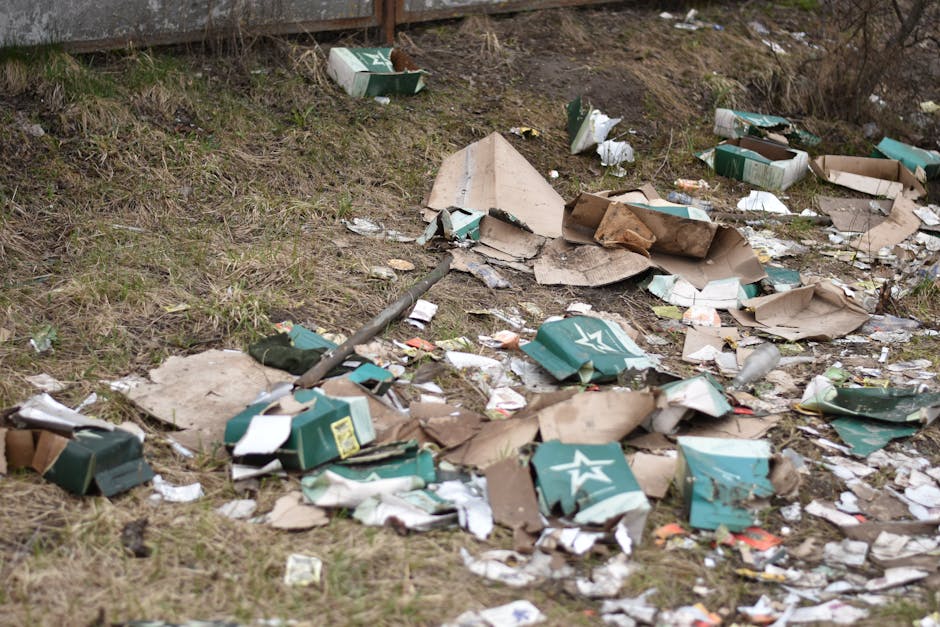 A close-up view of a person wearing a white glove, holding a white woven polypropylene sack filled with garden debris, including small branches, leaves, and gardening waste. The debris appears to cons